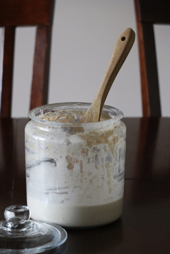 glass jar filled with sourdough starter and a wooden spoon